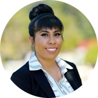 Rebecca Esparza, a twenty-something Latina with long straight black hair worn in a thick bun, smiles for a professional headshot. She has straight white teeth and wears a white collared shirt and black blazer.