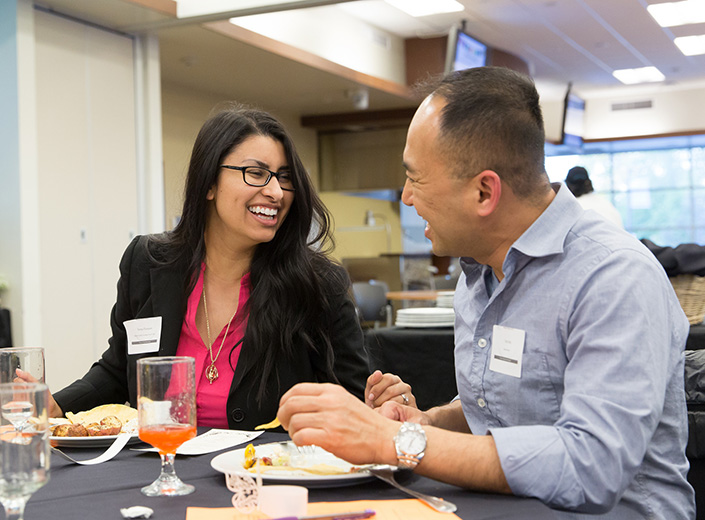 Two business people talking at a professional networking event. One is male and the other is female, they were business casual clothes and nametags.