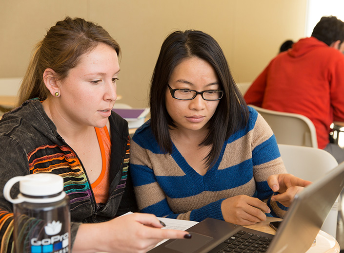 Two young women using a laptop computer in a classroom.