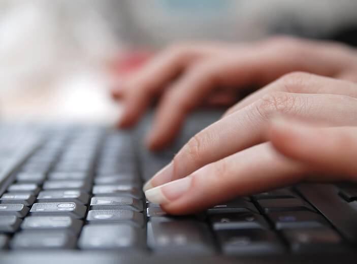 Woman's hands typing on laptop keyboard.