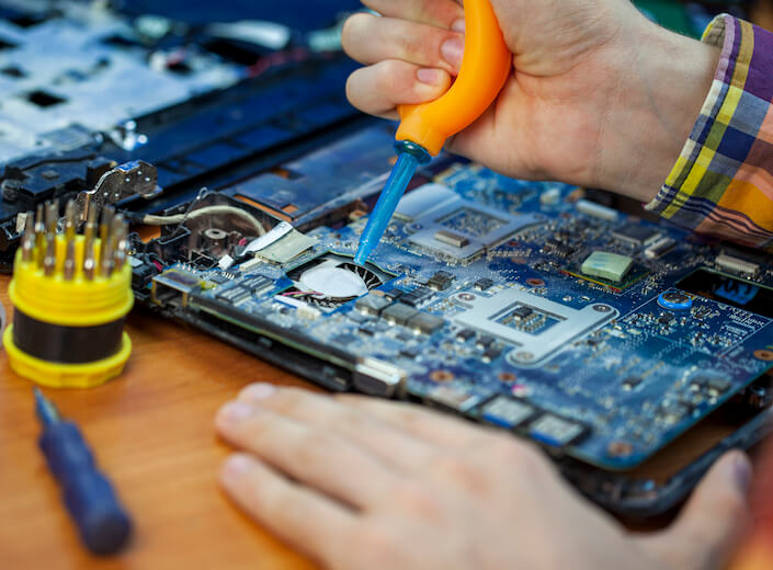A man's hands work on a circuit board with a screwdriver.