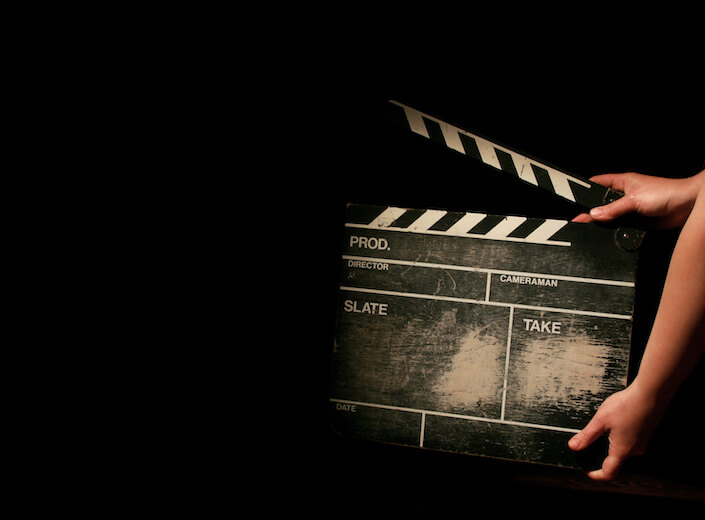 Hands hold a director's clapboard sign against black background insinuating a film shoot is in progress.