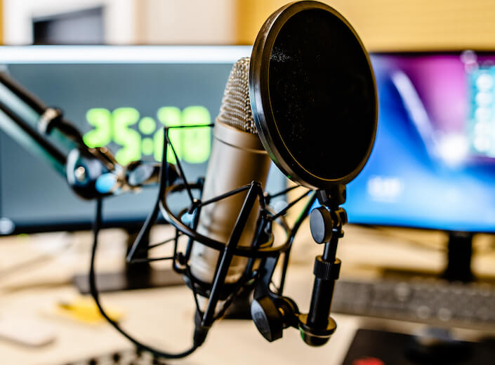 A close-up of buttons and controls in a music studio. A standing microphone is central object in the picture.