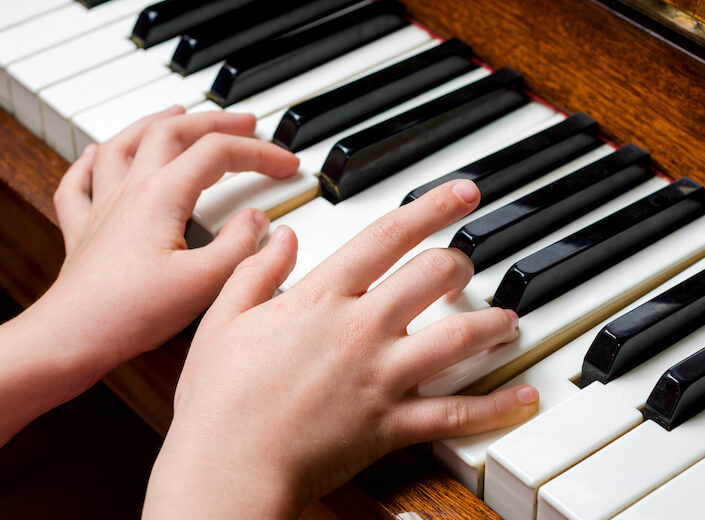 A child's hands are pictured on the keys of a piano.