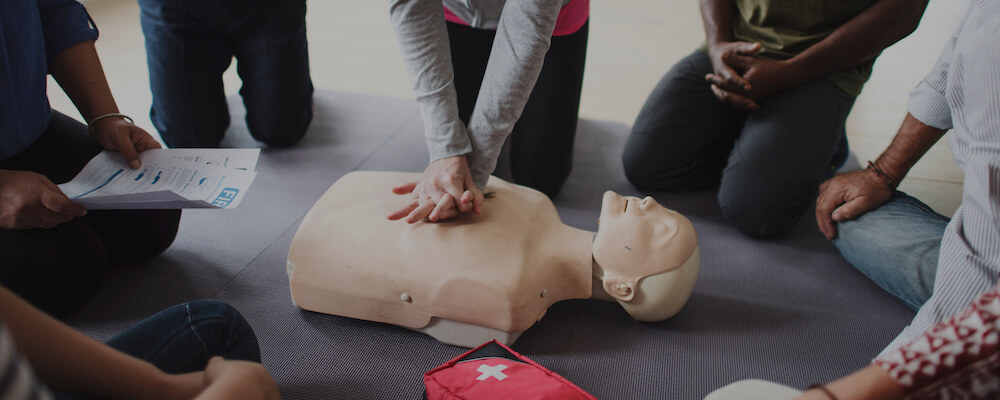 Students demonstrate CPR moves on a dummy in a semi-circle.
