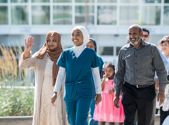 Young woman with headscarf walks with her family at her nursing graduation.