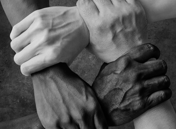 Different shades of skin - four hands grip each other in a rectangle shape.