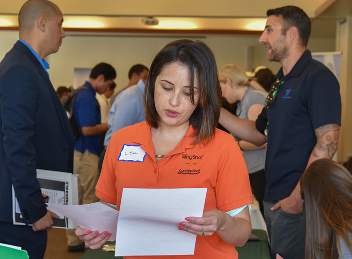Young woman in orange polo shirt looks at papers.