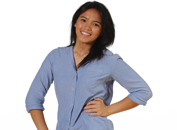 Female student of Asian descent poses in a long-sleeve blue button-down shirt against white background.