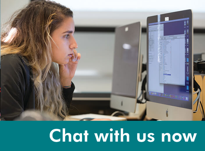 A young woman with curly light brown hair and tan skin is working at a computer on a college campus. "Chat with Us" is written in white text acrosss a teal strip on the bottom of the graphic.