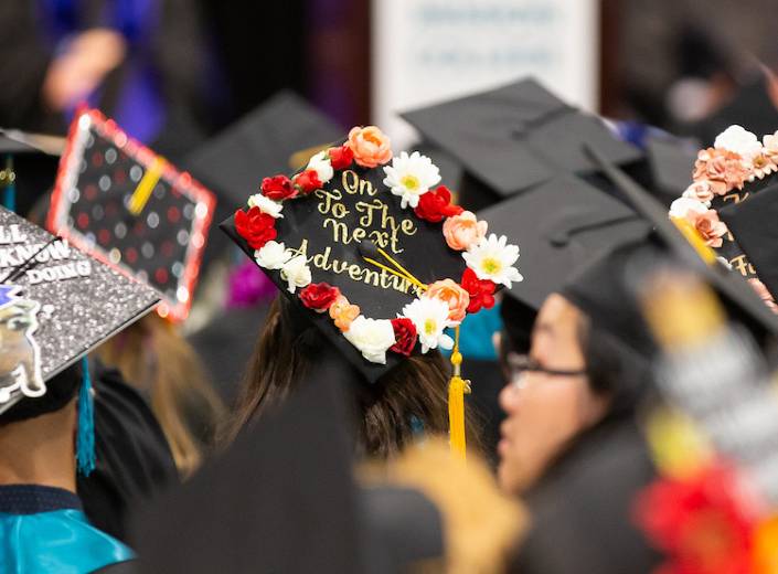Students are pictured from behind in a crowd in their caps and gowns.