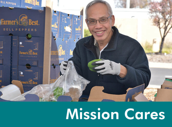 Vegetables are shown being distributed an outdoor event by an older man with short grey hair and square glasses Second Harvest. Across the bottom of the image "Mission Cares" is written in white text across a teal strip.