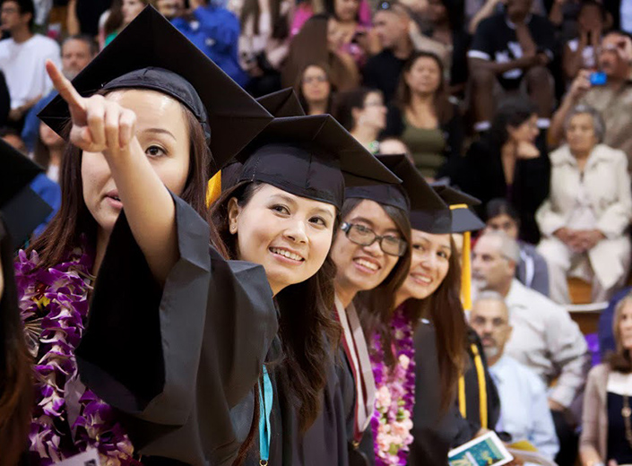Students are pictured from behind at commencement in their decorated black cap and gowns.