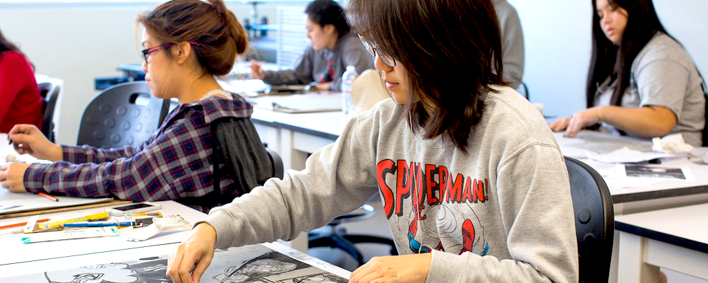 Asian-American female students work at a long desk in an art class.