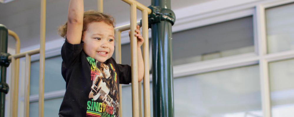 Young male child on playground equipment with curly blonde-ish hair uses jungle gym.