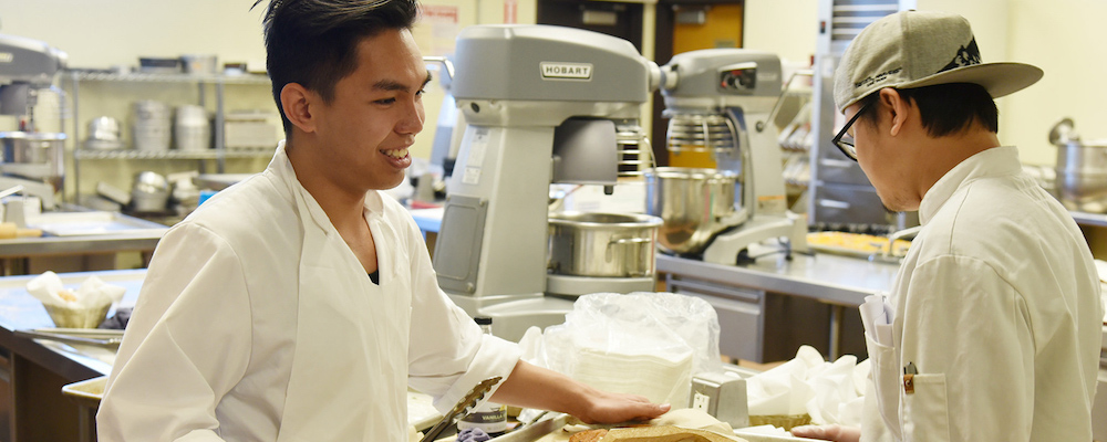 Student in white chef clothes cooking in industrial kitchen.