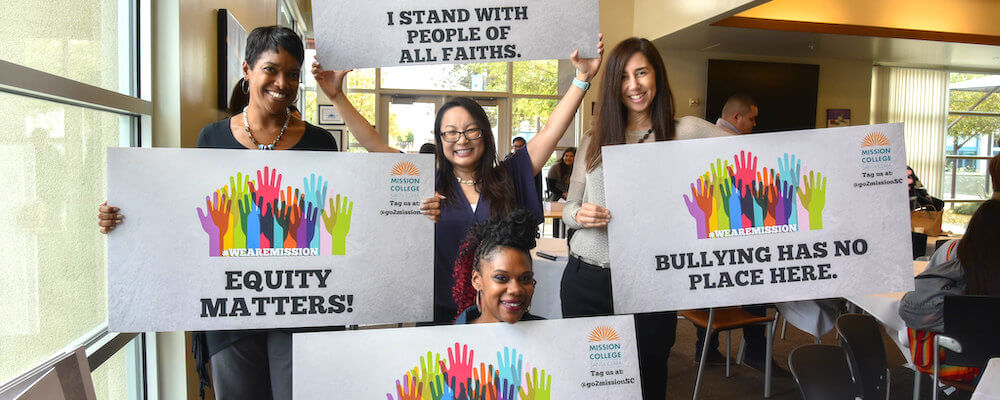 A group of students pose in a classroom holding signs that read "I support all women" etc.