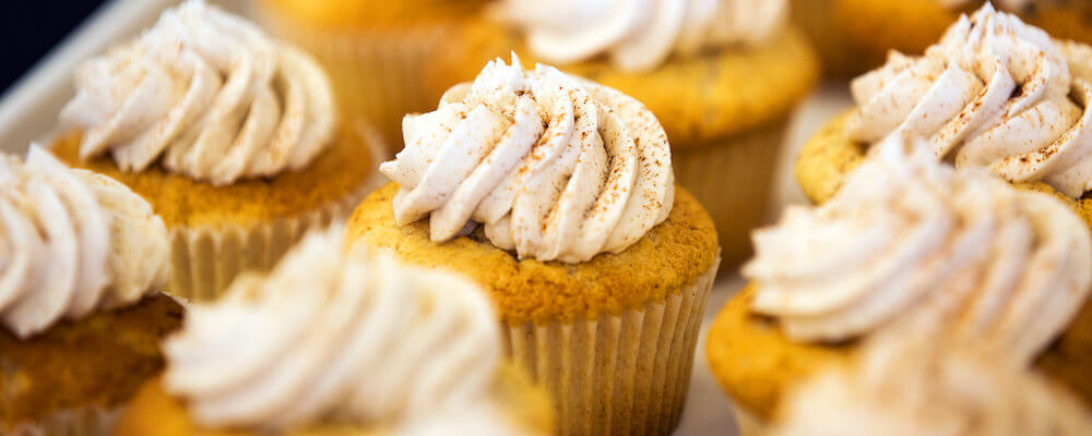 A tray of cupcakes is pictured, they have white frosting with cinamon sprinkled over them.