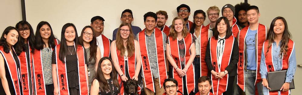 A group of students with bright orange MESA sashes poses in a group.