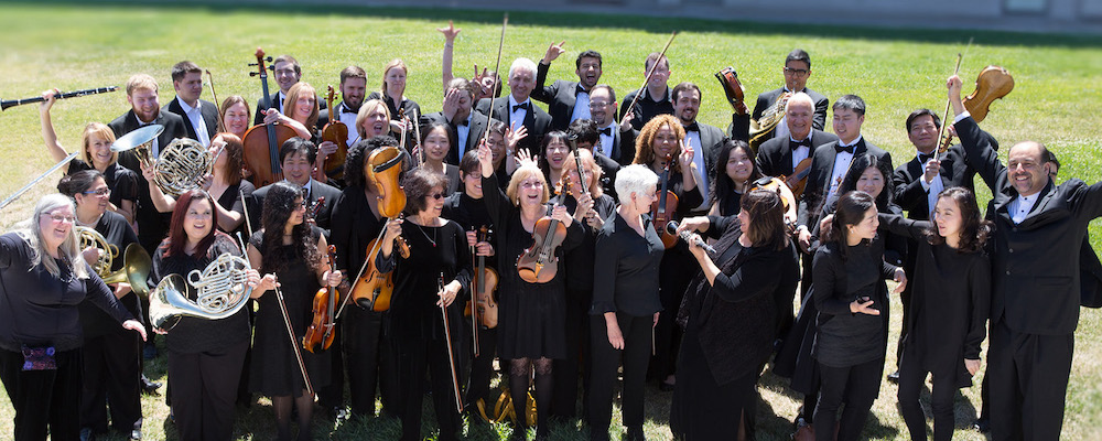 Members of the Mission Symphony pose in black with their instruments on the lawn.