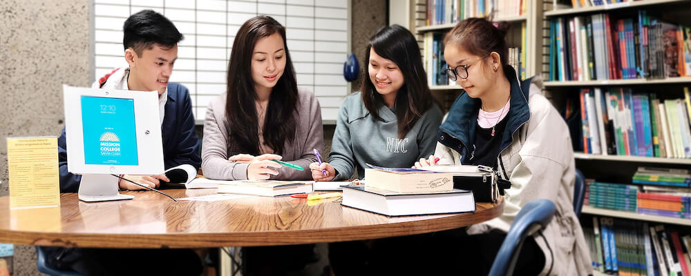 Four students of Asian descent work at a table in the library.